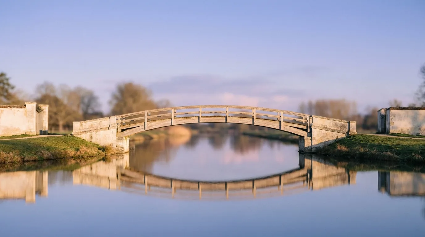 A footbridge arcing over calm water at golden hour — two banks, gently connected.